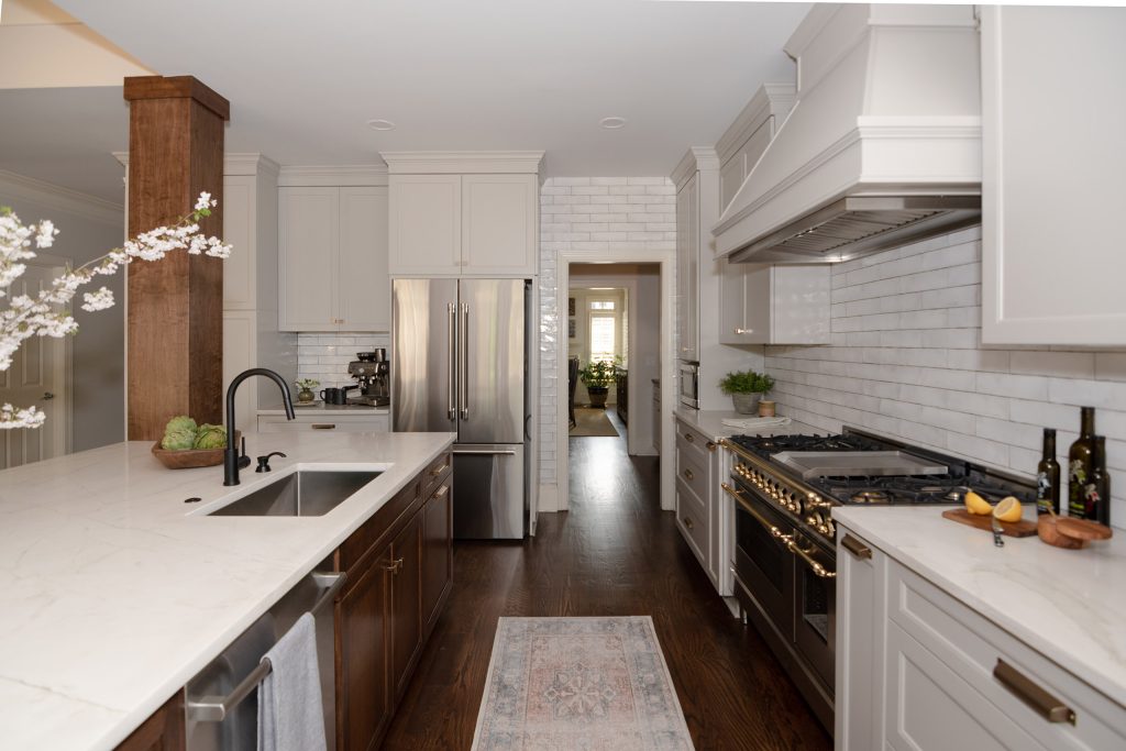 Custom kitchen with white and walnut mixed cabinetry, veined quartz counters, and a black-and-brass pro-style range.