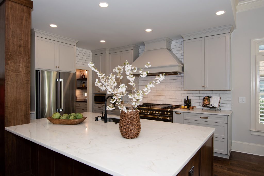 White quartz island with soft gray veining leading to a black-and-brass range, painted hood, and gray cabinets.