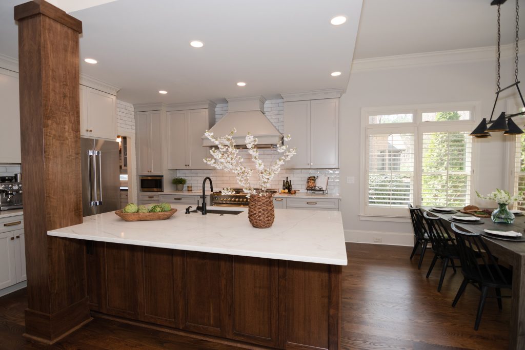 Open kitchen with a walnut island, gray cabinets, and painted hood, flowing to a dining area with a black-and-brass chandelier.