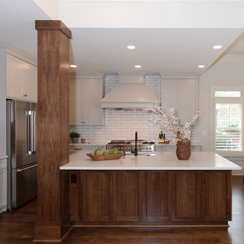 Custom kitchen with a walnut island, painted hood, black-and-brass range, and light-gray cabinets under white subway tile.