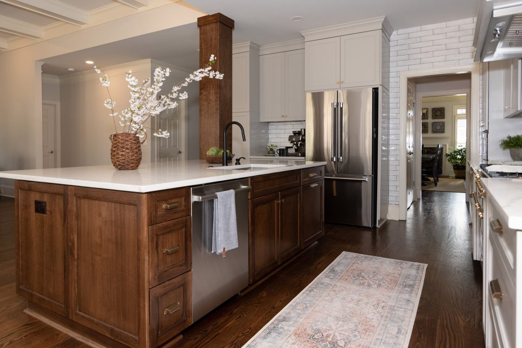 Walnut island with a stainless dishwasher and black faucet on a white quartz top, with a runner rug on oak floors.