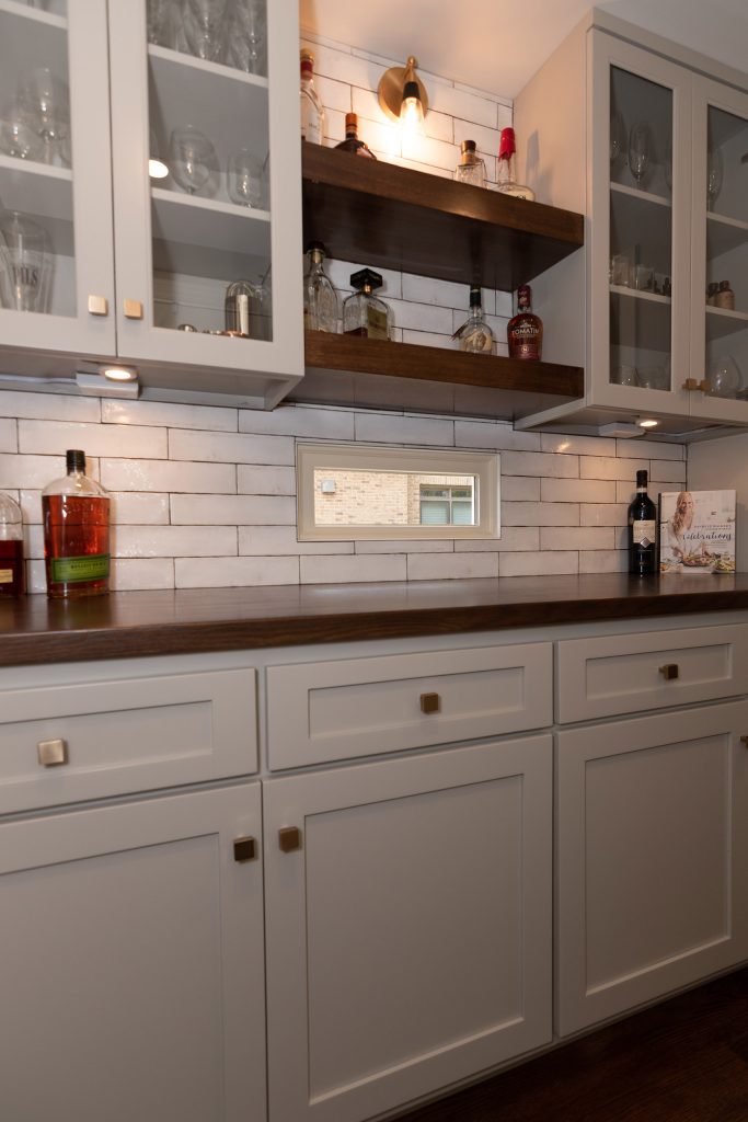 Kitchen view across a white quartz island toward a black-and-brass range, painted hood, and gray cabinets.