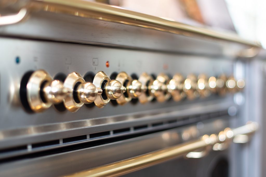 Close-up of a row of polished brass control knobs on a stainless professional range.