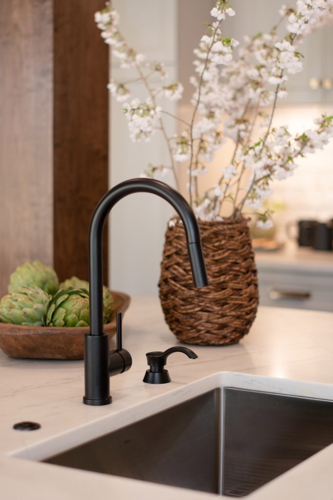 Black single-handle faucet and matching soap pump at a stainless undermount sink in a white quartz island.