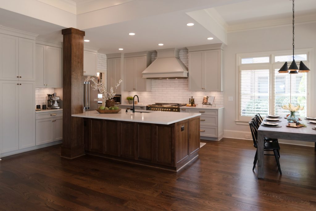 Open kitchen and dining space with a walnut island, gray cabinets, painted hood, and a black-and-brass chandelier over the table.