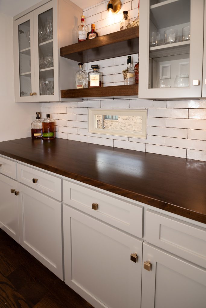 Butler's pantry with white shaker cabinets, walnut butcher-block counter, floating walnut shelves, and brass hardware.