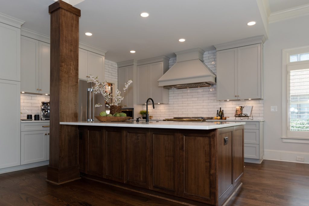 Walnut island with white quartz top in front of gray cabinets, a painted hood, and handmade white subway tile.