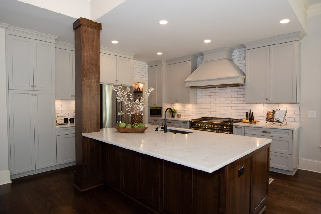 Walnut island with white quartz counter, gray perimeter cabinets, black-and-brass range, and painted hood over white subway tile.