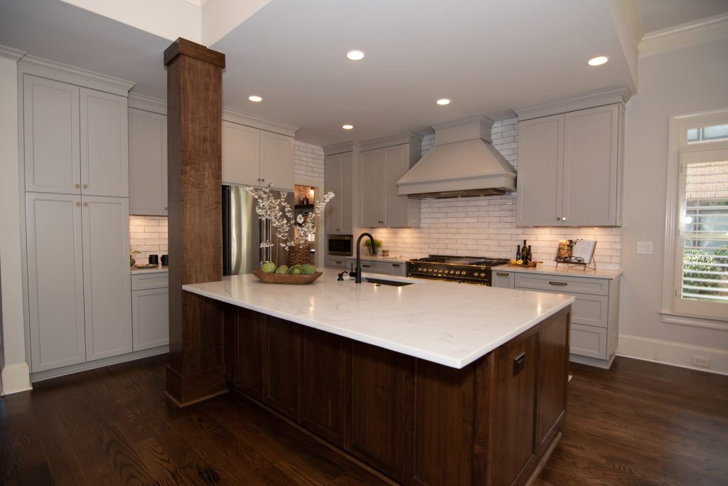 Custom kitchen with a walnut island, black-and-brass range, painted hood, and light-gray cabinets under white subway tile.