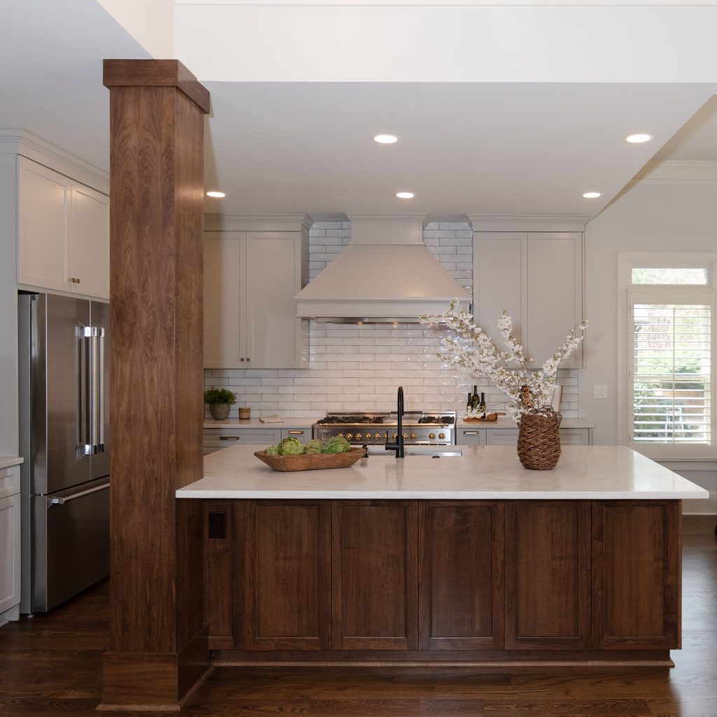 Walnut island with a white quartz top facing a black-and-brass pro range, painted hood, and white subway backsplash.