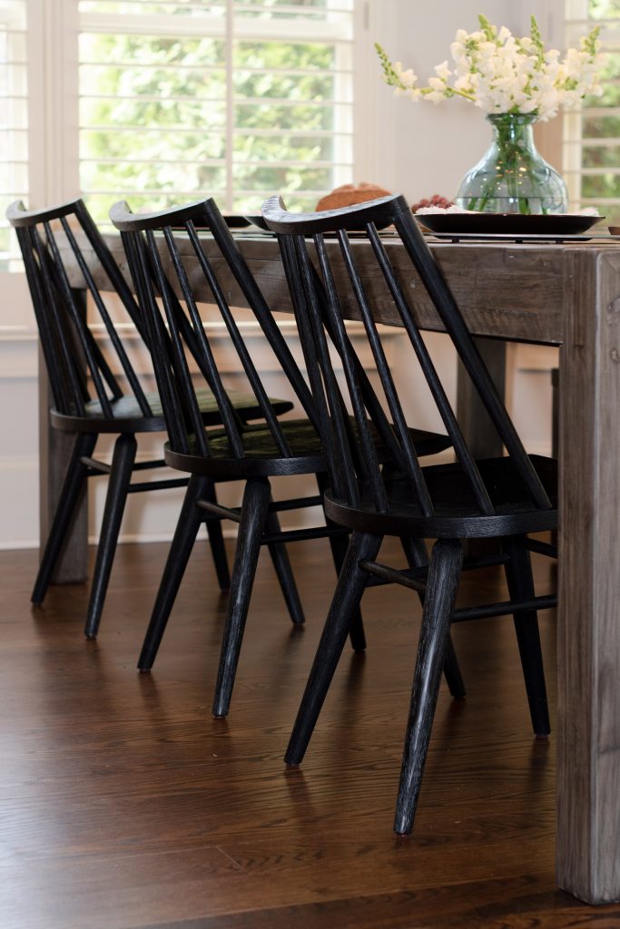 Three black spindle Windsor chairs pulled up to a weathered reclaimed-wood table on warm oak flooring.
