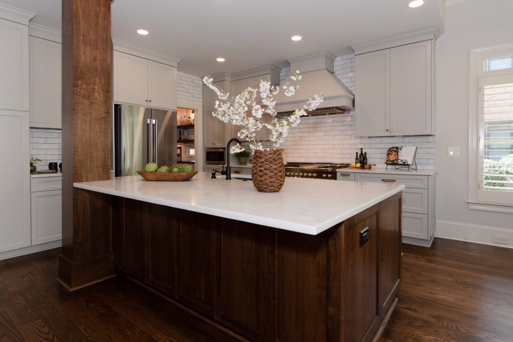 Walnut island with white quartz counter, walnut column, painted hood, and black-and-brass range against gray cabinets.