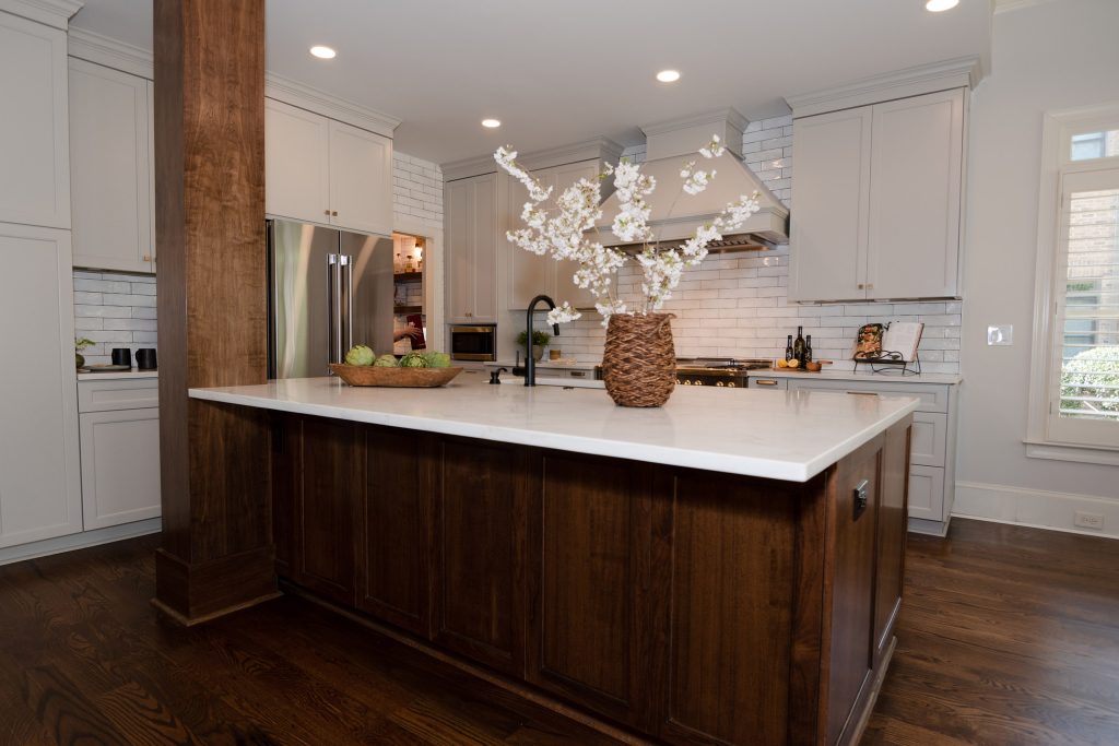 Walnut island with white quartz top, gray perimeter cabinets, painted hood, and a black-and-brass range in white subway tile.