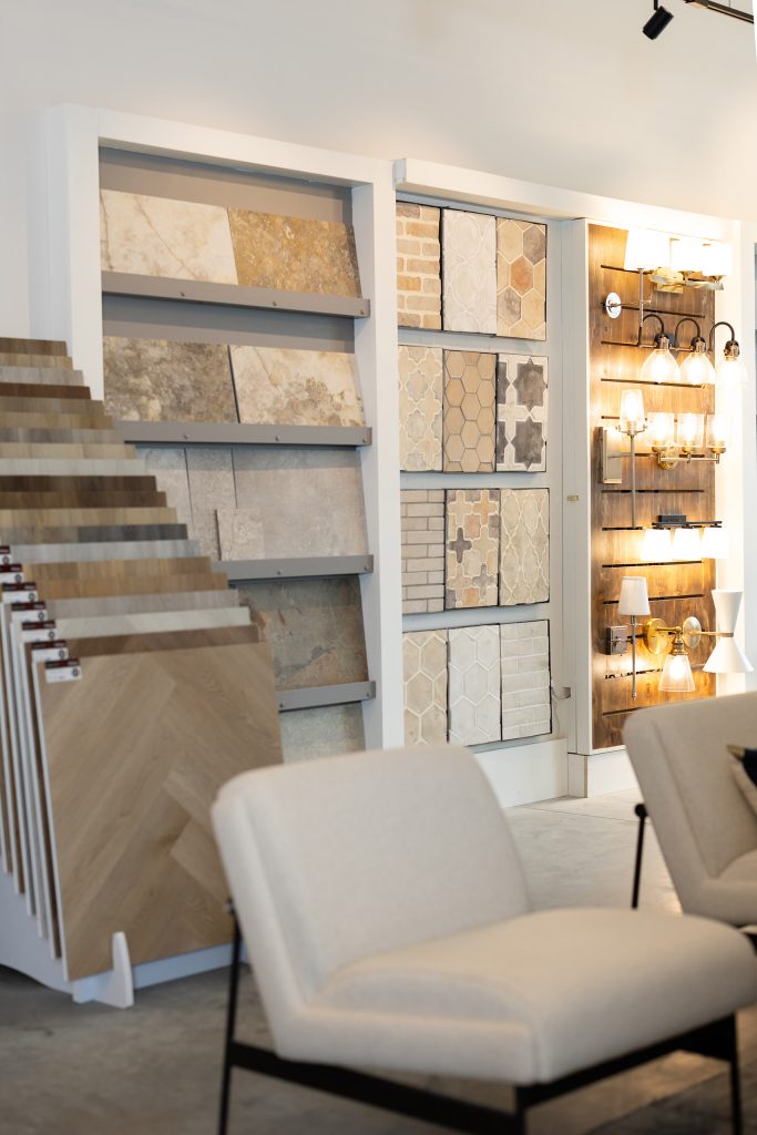 Sample display of stone-look large-format tile, arabesque and hexagon tiles, a herringbone wood flooring rack, and a lit sconce board.