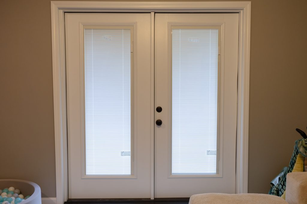 White interior French doors with built-in mini blinds set in a taupe wall.