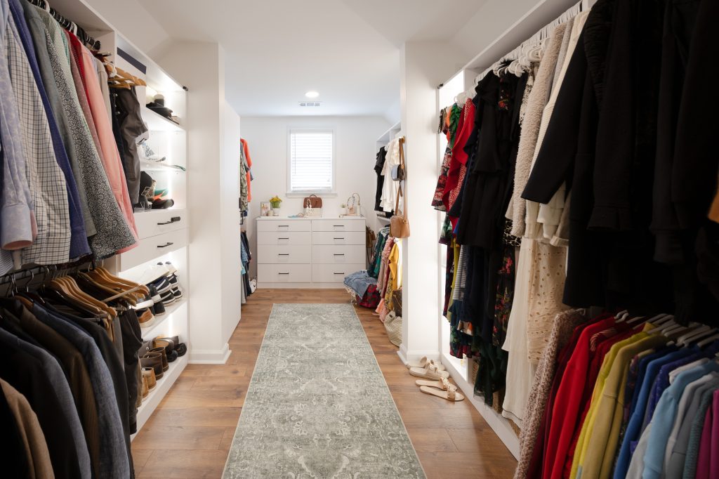 Walk-in closet corridor lined with white built-in rods and shelves, a runner rug, and a dresser under a window.