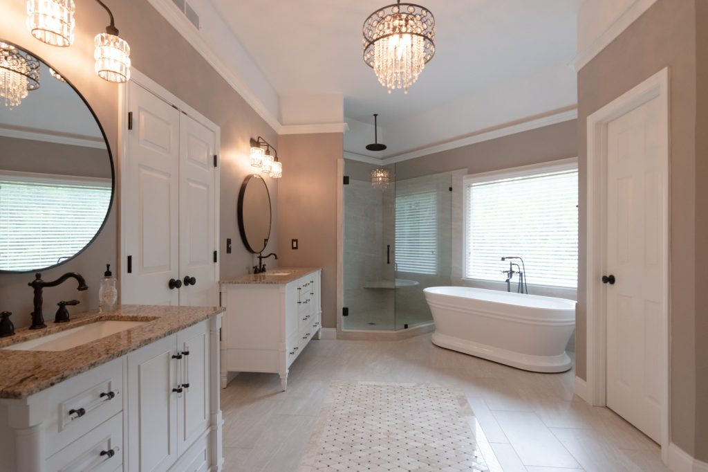 Transitional primary bathroom with white vanities, speckled quartz counters, a freestanding tub, corner shower, and a crystal drum chandelier.