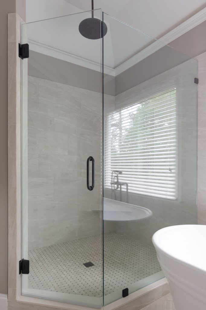 Frameless neo-angle glass shower with a black rain head, marble-look tile walls, and a basketweave marble mosaic floor.