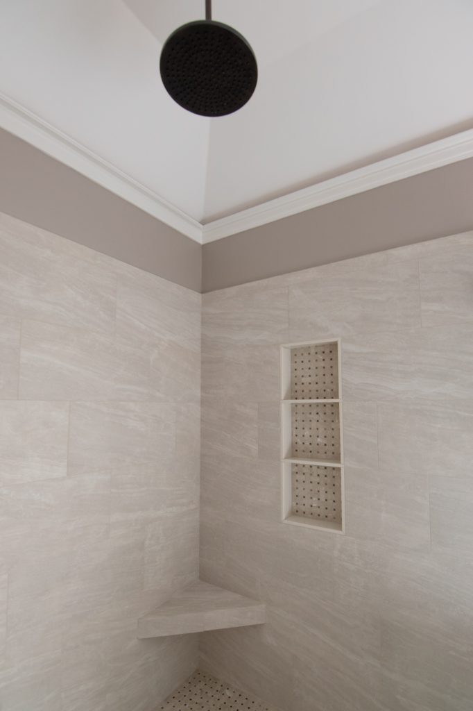 Matte-black ceiling rain shower head over a corner bench seat and triple niche in cream marble-look tile.