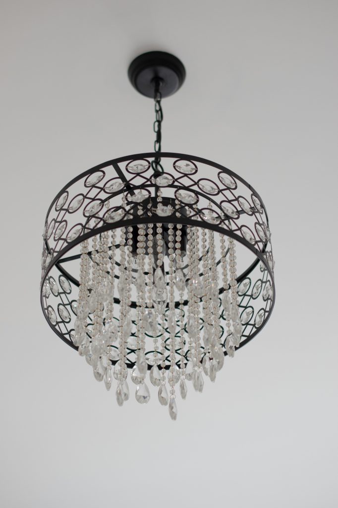 Oil-rubbed bronze drum chandelier with oval crystals and cascading crystal strands hanging from a white ceiling.