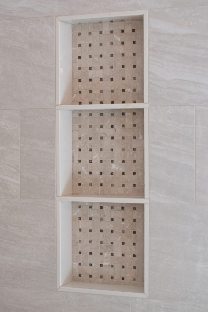 Triple shower niche backed with cream marble basketweave mosaic and dark accent dots, framed in large-format marble-look tile.
