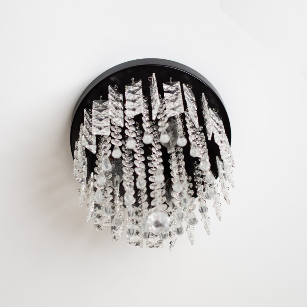 Crystal flush-mount ceiling light with cascading clear crystals on a black round canopy against a white ceiling.