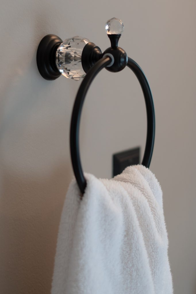 Oil-rubbed bronze towel ring with a faceted crystal accent, holding a plush white towel against a pale wall.