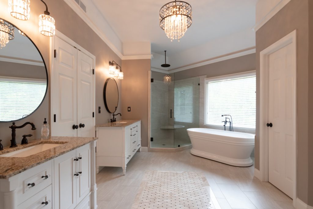 Timeless primary bath with white vanities, a freestanding tub, corner glass shower, and a crystal drum chandelier over marble-look tile.