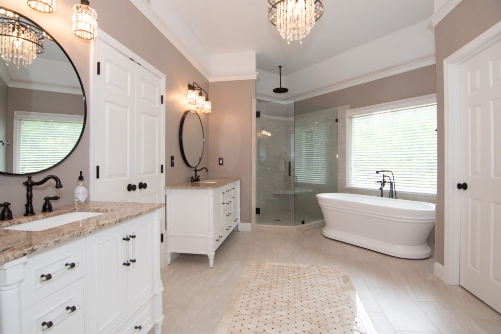 Luxury bathroom with two white vanities, black round mirrors, crystal sconces, a corner glass shower, and a soaking tub.