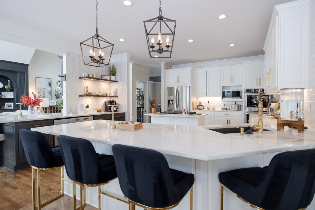Large quartz island with black velvet gold-legged barstools under twin lantern pendants in an open kitchen.