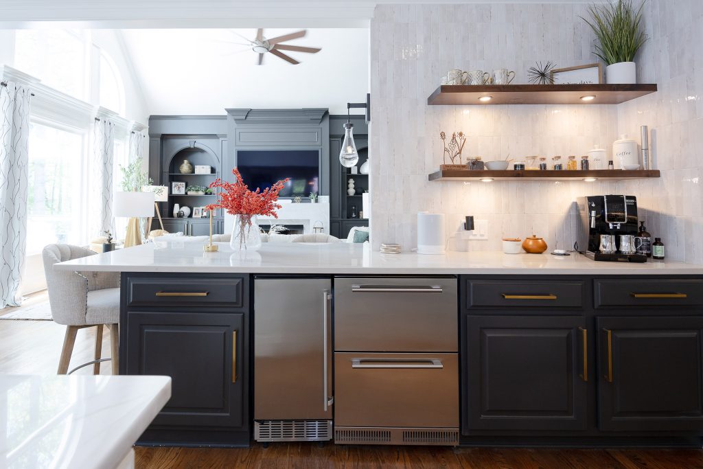 White kitchen with a gas cooktop island, veined quartz counters, lantern pendants, and a stone-clad TV nook.