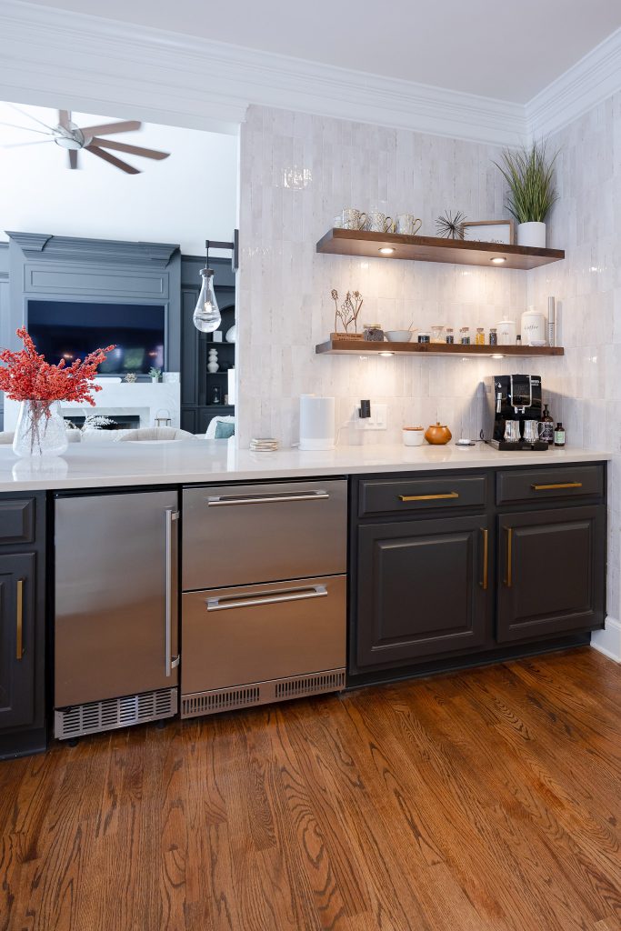 Coffee bar with charcoal cabinets, gold pulls, floating wood shelves, zellige-look tile, and stainless drawers.