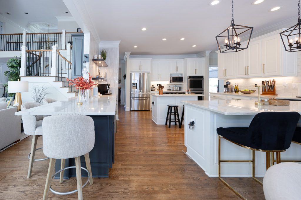 Dual-island kitchen with white cabinets, a navy island, gold hardware, lantern pendants, and mixed barstools.