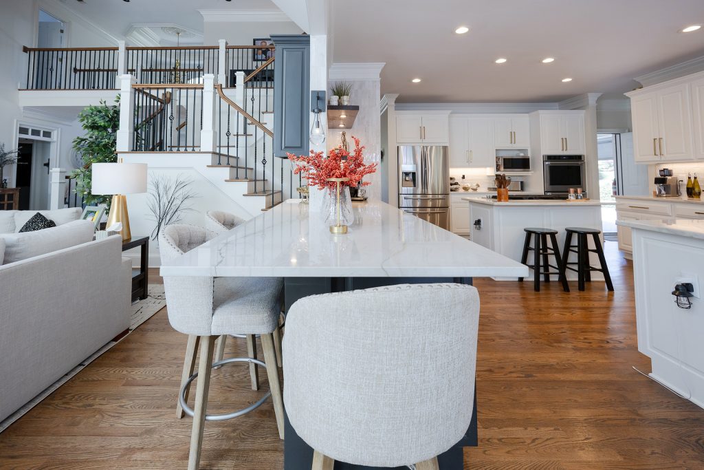Veined quartz island with gray upholstered barstools opening to a white kitchen with navy island and black stools.