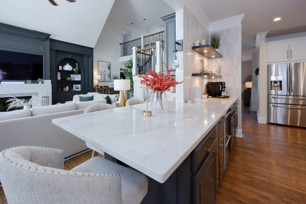 Kitchen peninsula with veined quartz top, gray upholstered barstools, dark cabinetry, and a stainless beverage center.