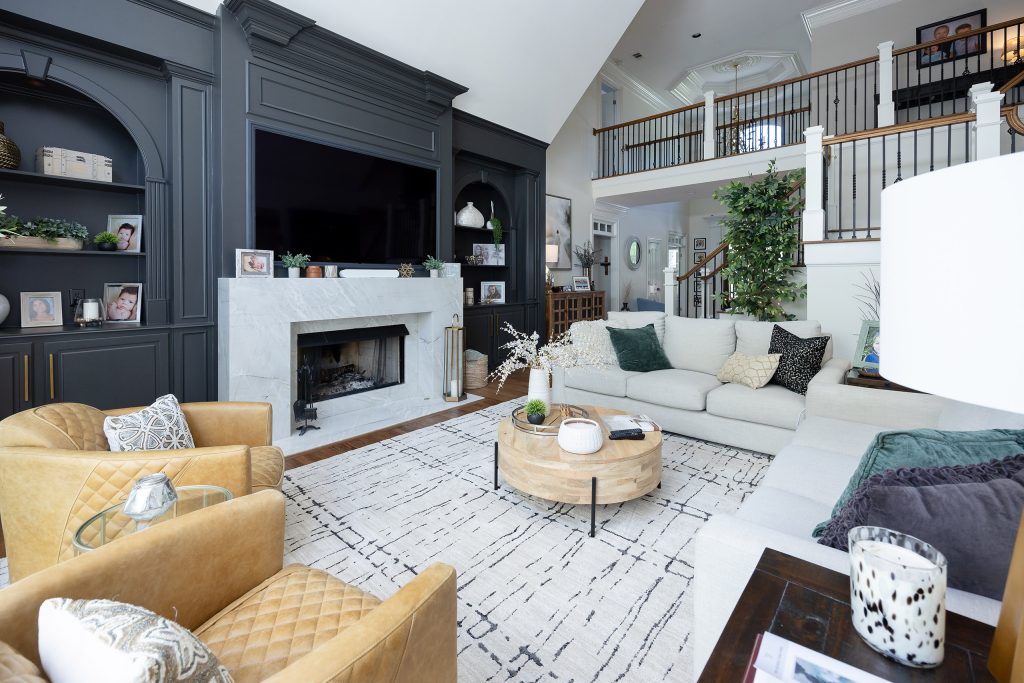Family room with charcoal built-ins, marble fireplace, linen sectional, tan chairs, and staircase to a loft.
