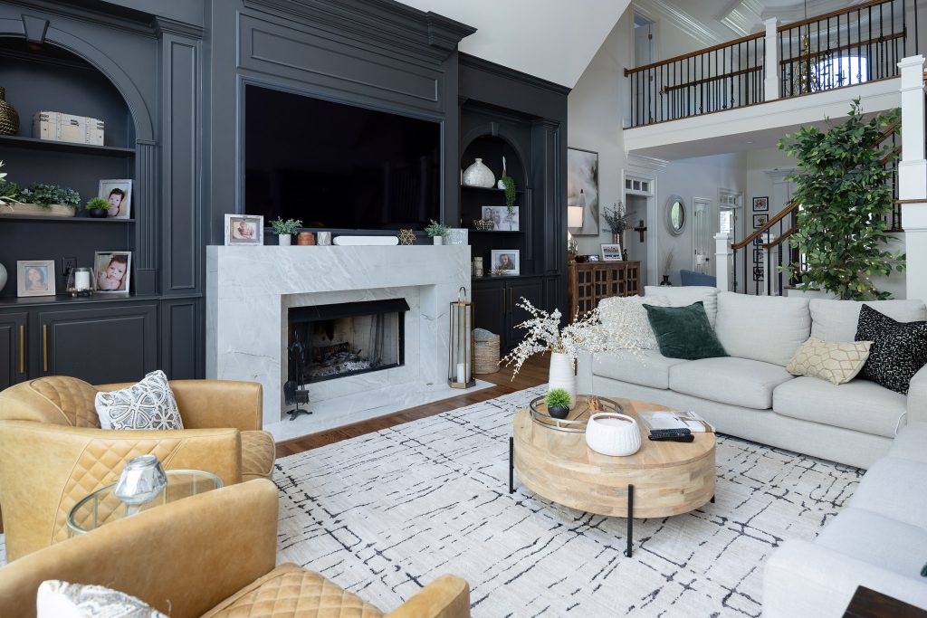 Living room fireplace wall in charcoal built-ins with marble surround, tan leather chairs, and a wood coffee table.
