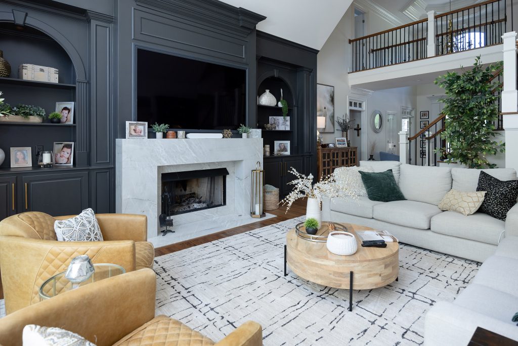 Family room with charcoal built-ins, marble fireplace, quilted tan chairs, linen sofa, and loft railing above.