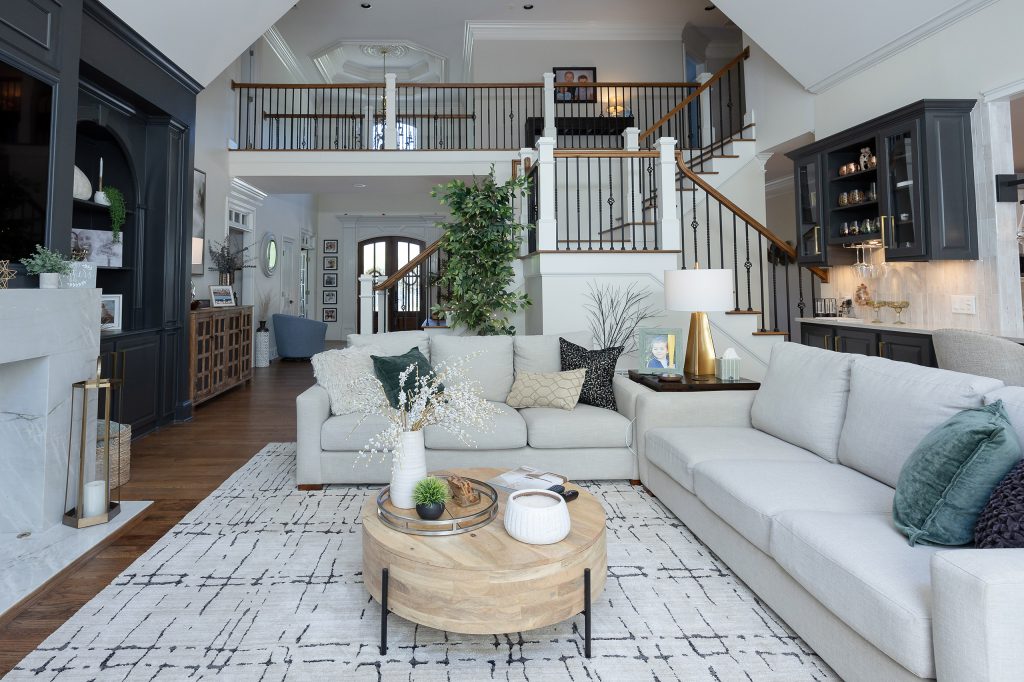 Two-story great room with iron-baluster staircase, gray sectionals, wood coffee table, and a dark built-in wet bar.