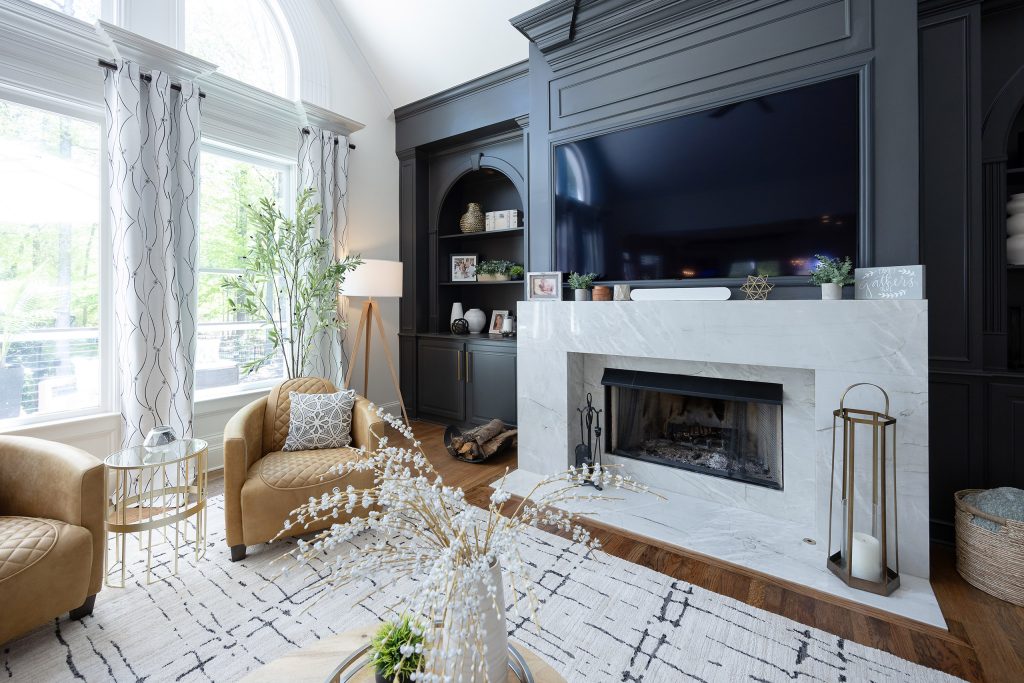 Fireplace corner with veined marble surround, mounted TV, arched windows, and quilted tan leather chairs.