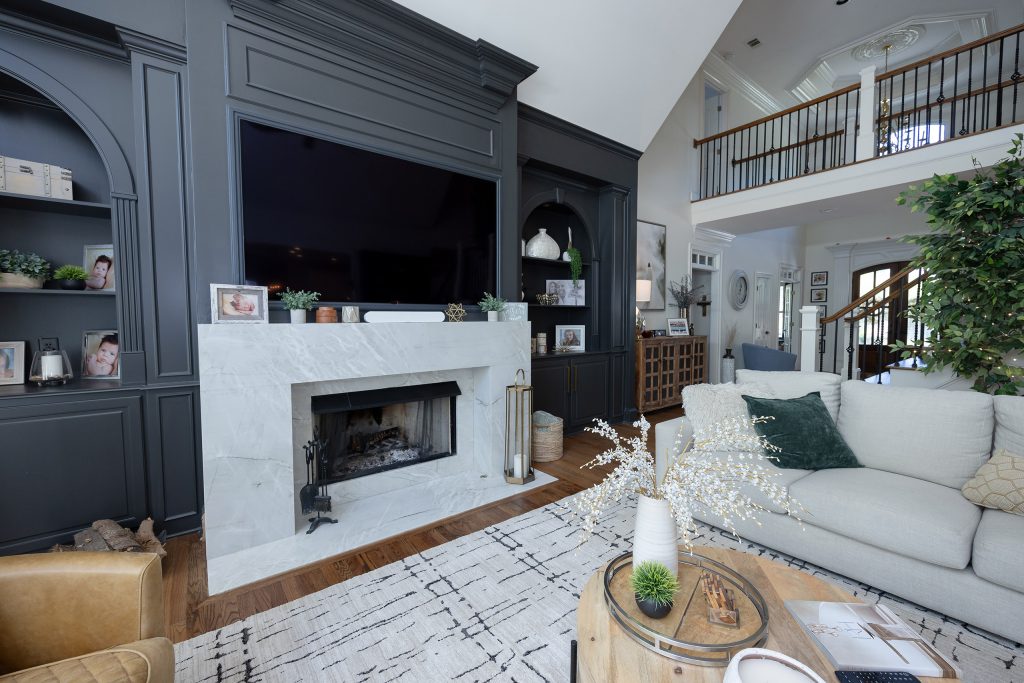 Family room with charcoal built-ins, veined marble fireplace, linen sofas, and a round wood coffee table.