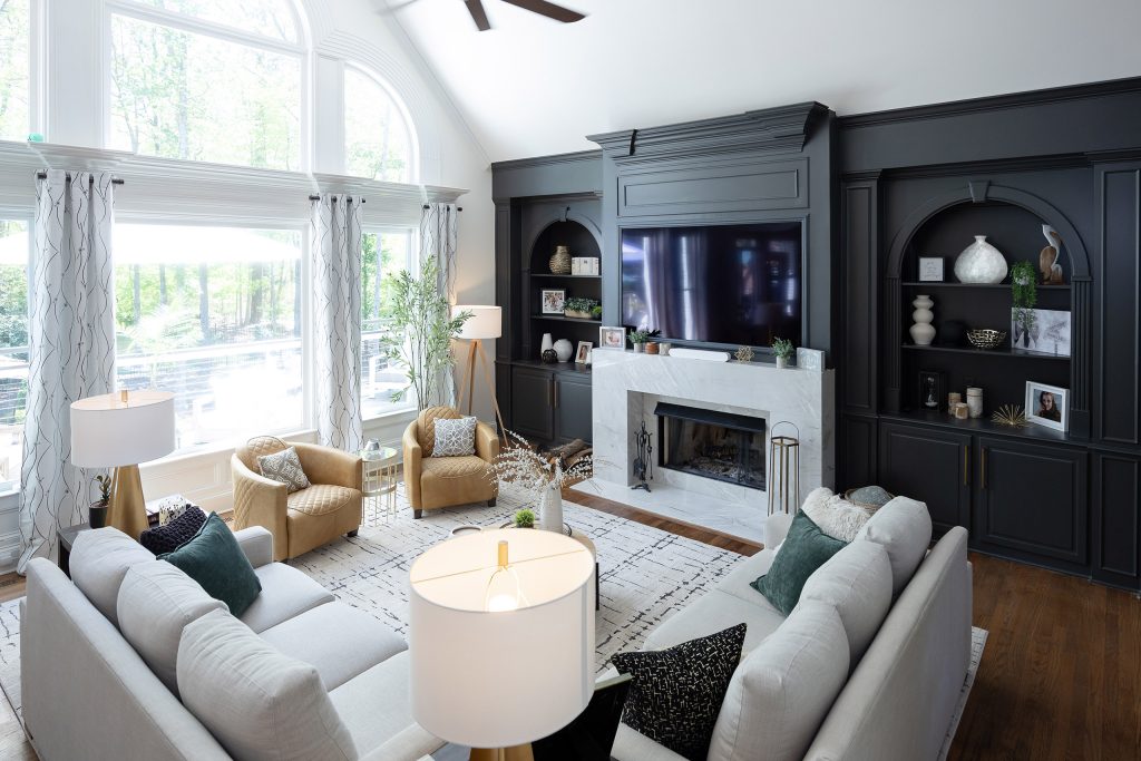 Vaulted living room with tall arched windows, charcoal built-ins, marble fireplace, and gray and tan seating.