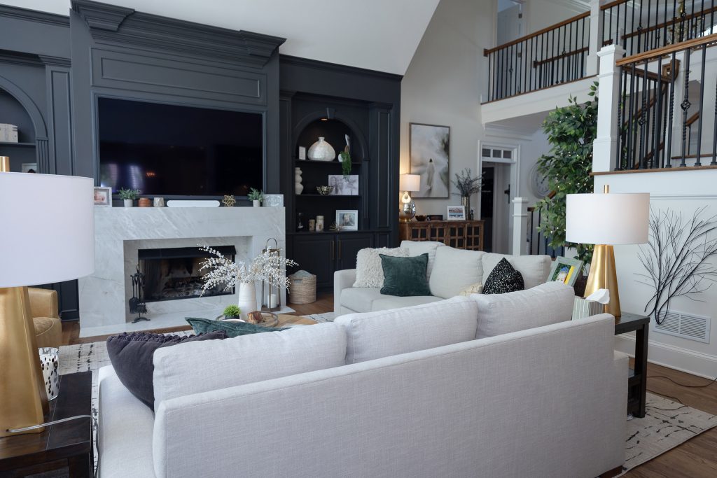 Two-story family room with charcoal built-ins, marble fireplace, white sofas, and an iron-balustrade staircase.