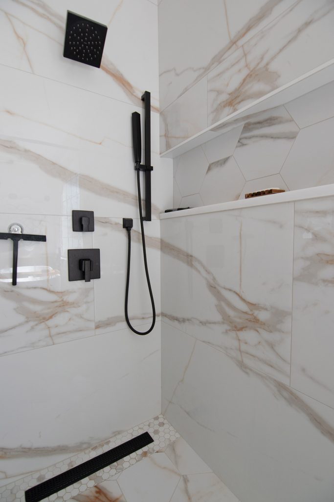 Walk-in shower clad in dramatic calacatta marble-look porcelain with matte-black fixtures and a hex-tile niche.