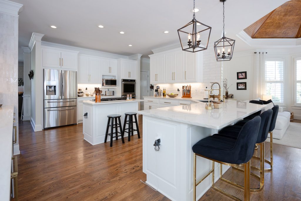 Open white kitchen with two islands, veined quartz counters, navy barstools, and a coffered wood cupola ceiling.