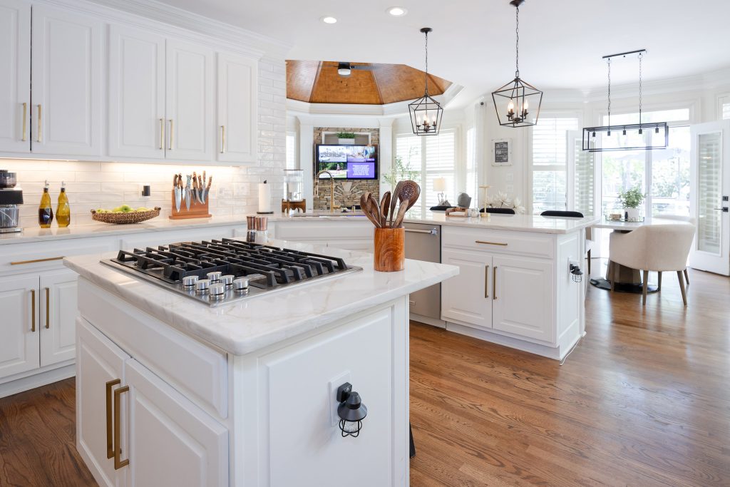 White kitchen corner with subway tile, gold hardware, veined quartz counters, gold faucet, and black stools.