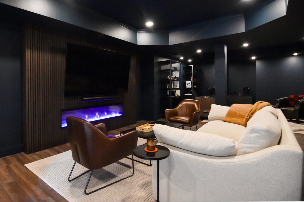 Finished basement lounge with a linear electric fireplace, slatted wood media wall, and cream sectional seating