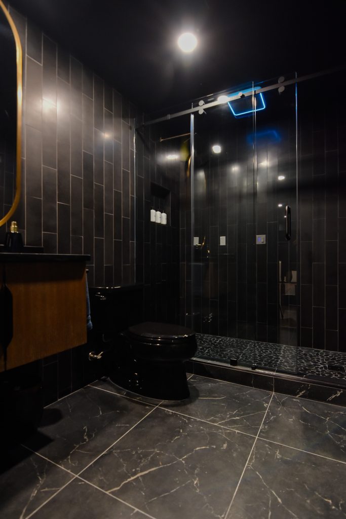 Basement full bathroom with a glass-enclosed walk-in shower, black tile walls, and marble-look floor tile