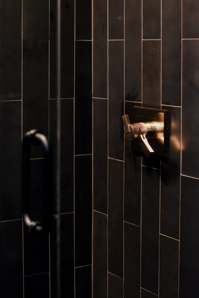 Black vertical shower tile with a bronze shower valve trim and matte black grab bar