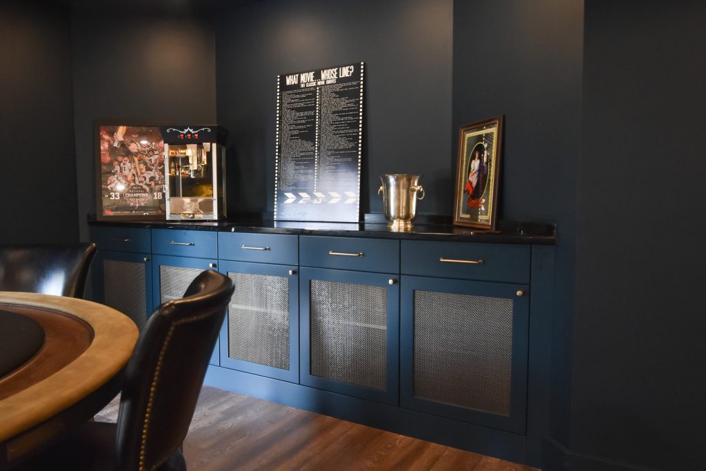 Basement game room with a poker table and custom blue cabinetry with metal mesh door fronts